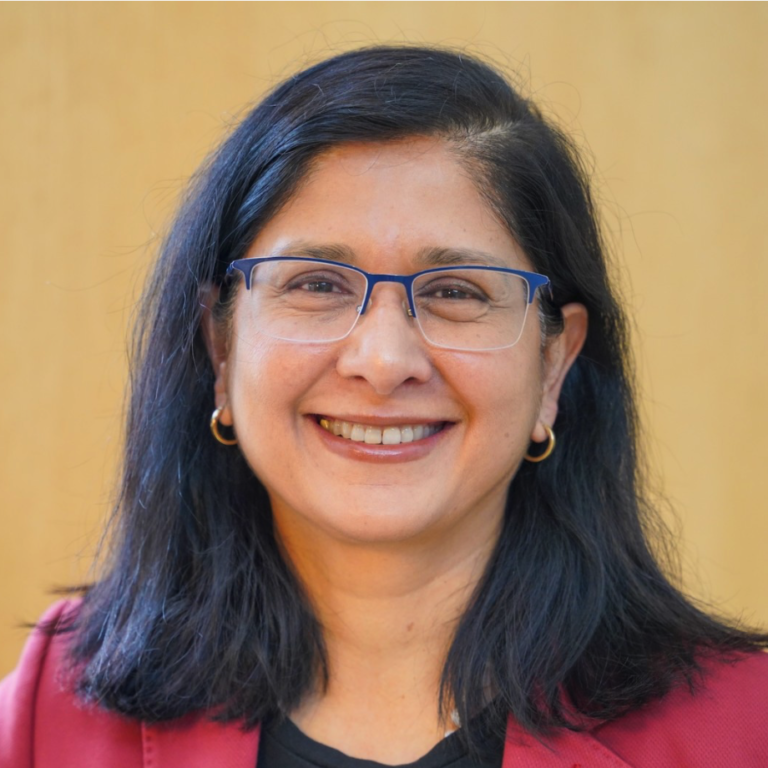 woman with dark hair and glasses smiling while wearing a red blazer